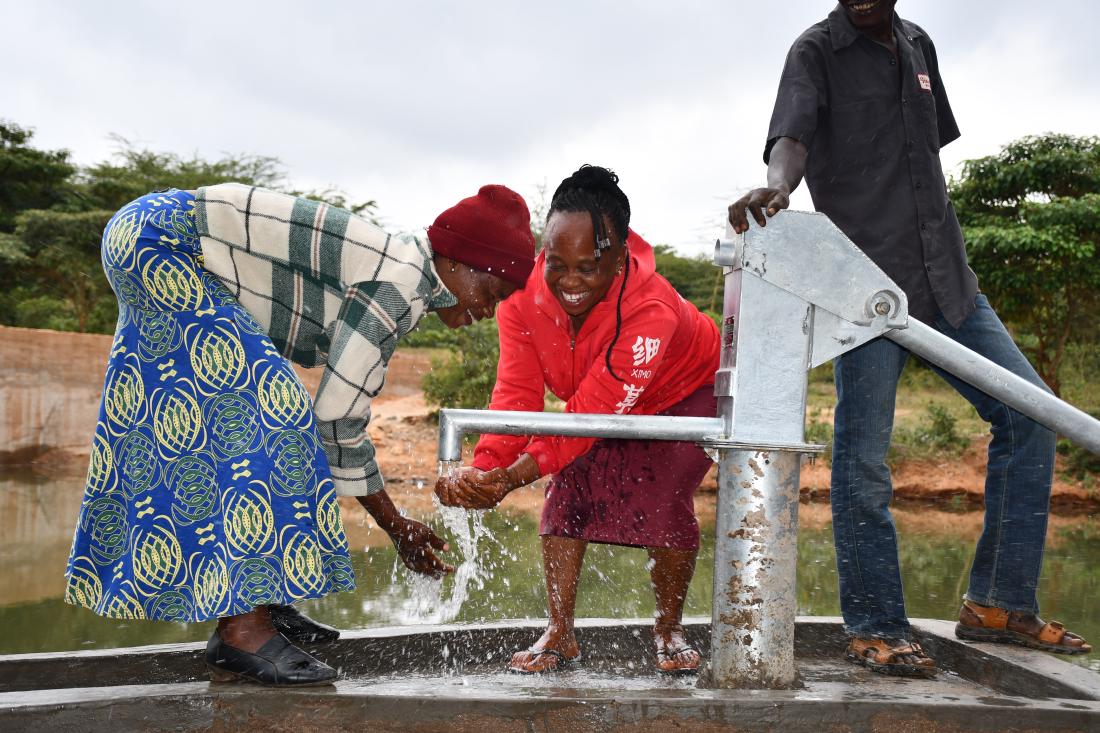 women pumping water from a sand dam